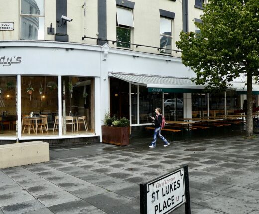 A corner restaurant with outdoor benches at the top of Bold Street, Liverpool, beside the St Lukes Place street sign
