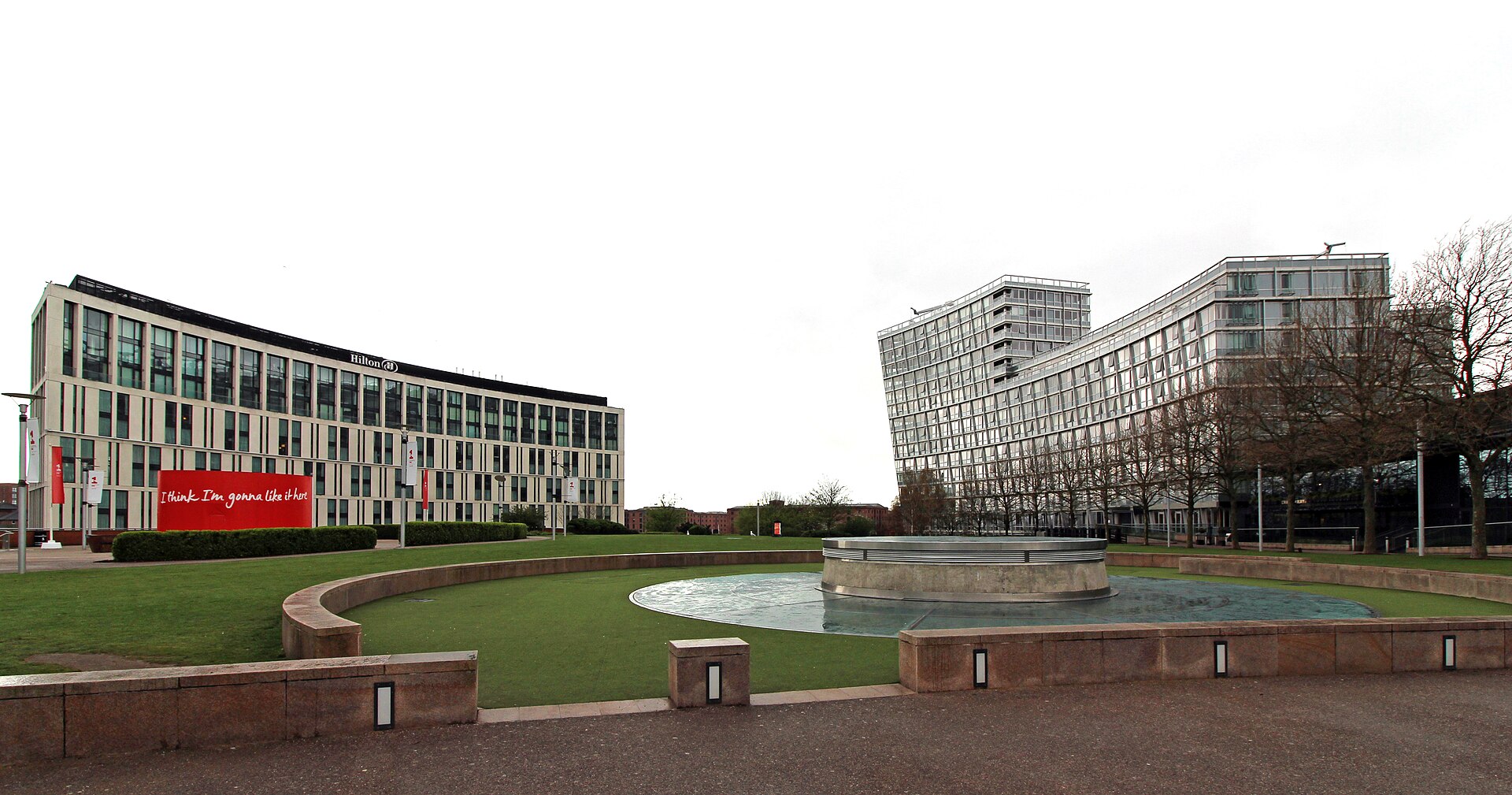 Competitive Socialising in Liverpool: Crazy Golf, Darts & Escape Rooms 3 Chavasse Park at Liverpool ONE, a lawn with a circular stone water feature, the Hilton hotel on the left and the curved glass One Park West apartments on the right
