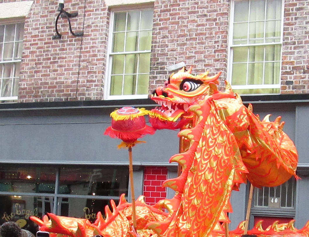 A red and gold Chinese dragon costume with a pearl on a pole, performing in front of brick buildings on Nelson Street, Liverpool, at Chinese New Year
