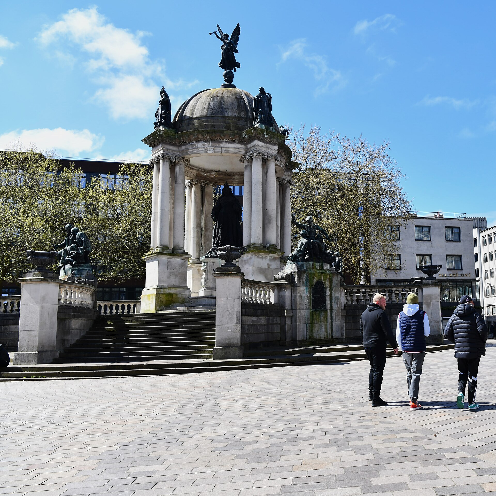 The Queen Victoria Monument in Derby Square, Liverpool, a domed stone rotunda with a winged figure on top and bronze statues at its base, under a blue sky