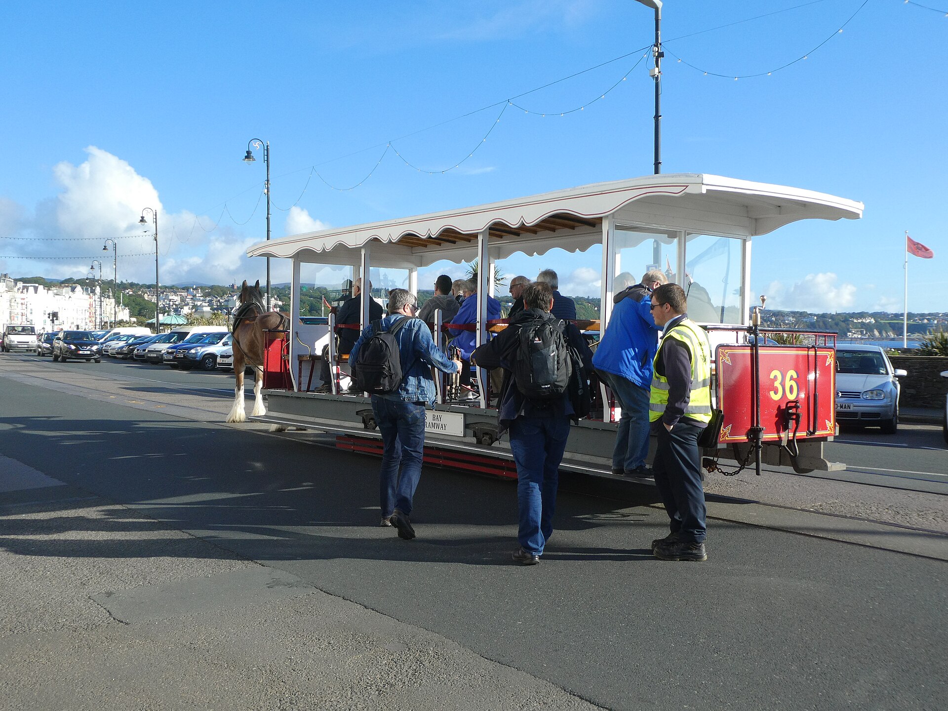 Isle of Man Ferry from Liverpool: Day Trips & Sailings 2 A horse-drawn tram, car number 36, with passengers boarding on Douglas promenade, Isle of Man, under a blue sky with festoon lights overhead