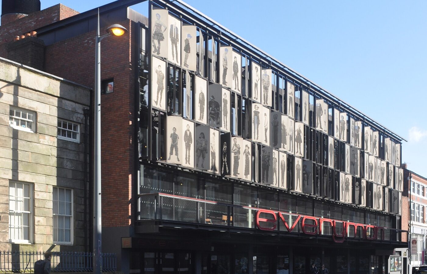 Liverpool Everyman & Playhouse: The City's Producing Theatres 5 The Everyman Theatre on Hope Street, Liverpool, its upper floors screened by metal panels bearing life-size portraits of local people, above a red Everyman sign