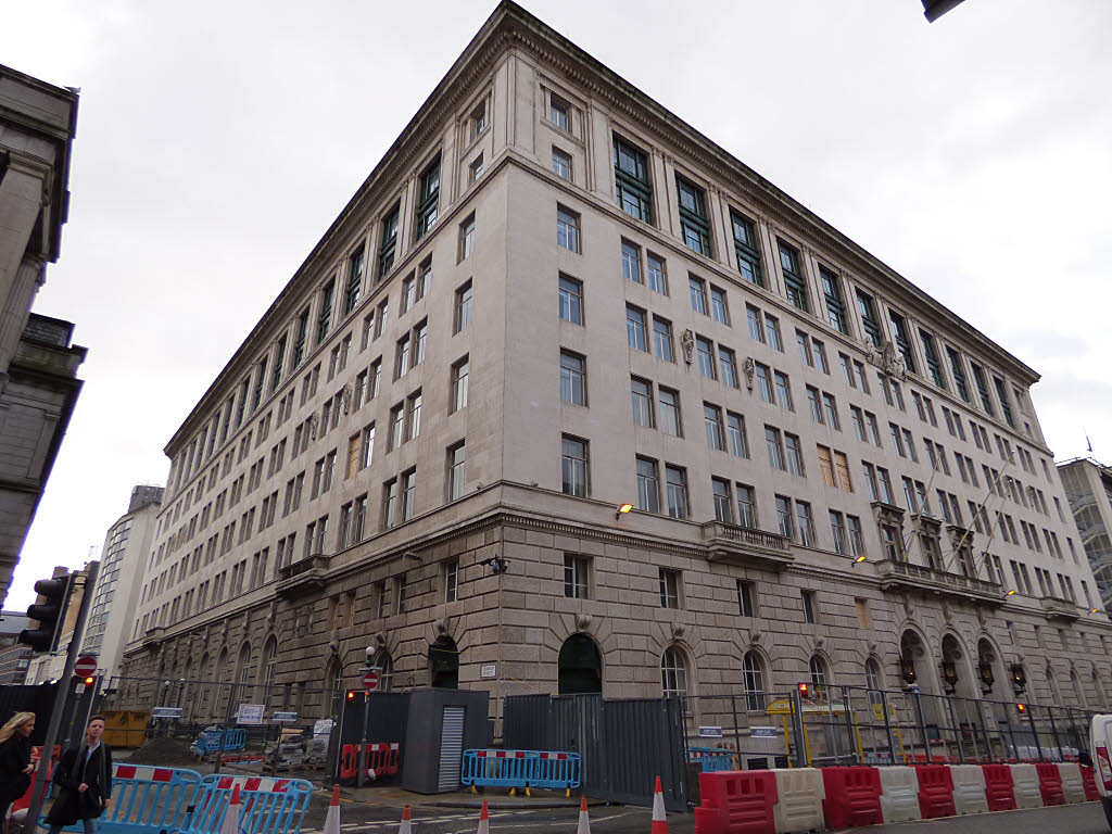 India Buildings on Water Street, Liverpool, a massive pale stone office block with rows of windows and arched ground-floor openings, with roadworks barriers in front