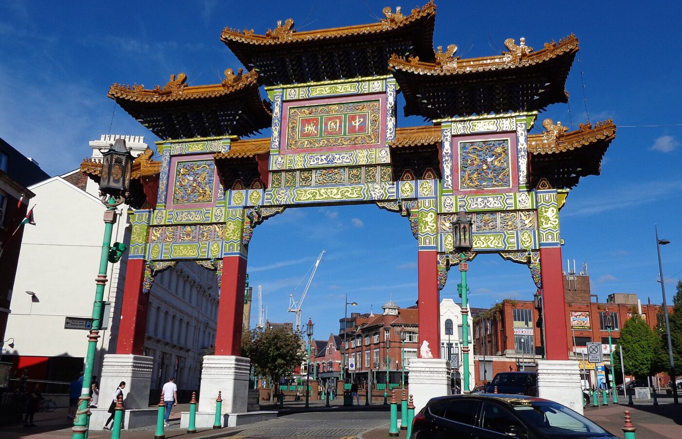 The ornate Chinatown arch in Liverpool, with gold-tiled roofs, red pillars and panels of carved gold dragons on green and blue, against a deep blue sky