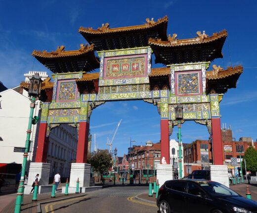 The ornate Chinatown arch in Liverpool, with gold-tiled roofs, red pillars and panels of carved gold dragons on green and blue, against a deep blue sky