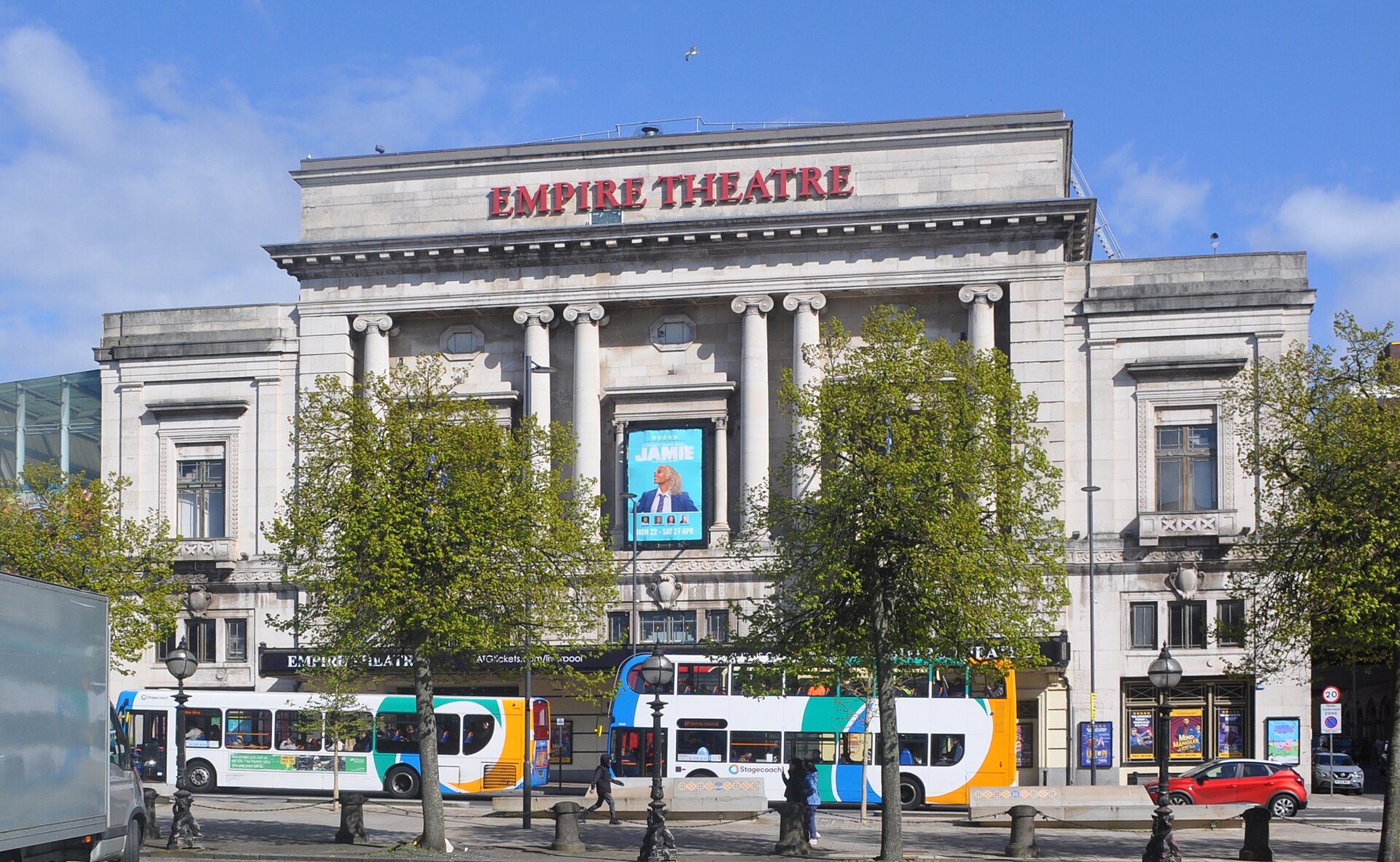 Liverpool Empire Theatre Guide: Seating, Shows & What to Know 3 The full stone façade of the Empire Theatre on Lime Street, Liverpool, with Ionic columns and red lettering, and double-decker buses passing in front