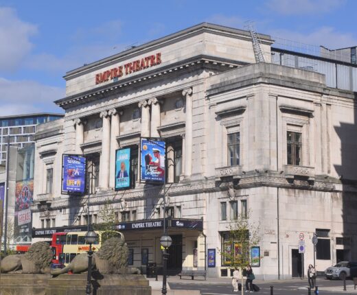 The stone front of the Empire Theatre on Lime Street, Liverpool, with show banners between its columns, seen past the stone lions of St George's Plateau