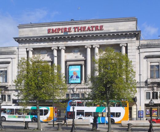 The neoclassical stone frontage of the Liverpool Empire Theatre on Lime Street with buses passing in front