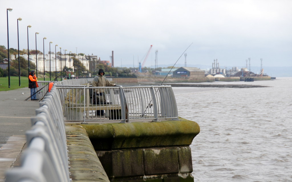 Lark Lane & Aigburth: Liverpool's Bohemian South End 2 People fishing from the railings of Otterspool Promenade beside the River Mersey, with the promenade path and lamp posts stretching into the distance