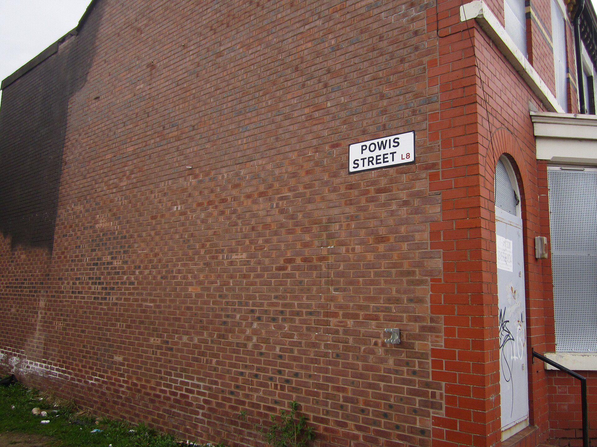 A white Powis Street L8 street sign on the brick gable end of a terraced house in Toxteth, Liverpool