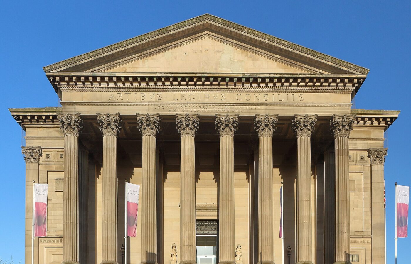The south portico of St George's Hall, Liverpool: eight fluted Corinthian columns under a pediment inscribed Artibus Legibus Consiliis, against a deep blue sky