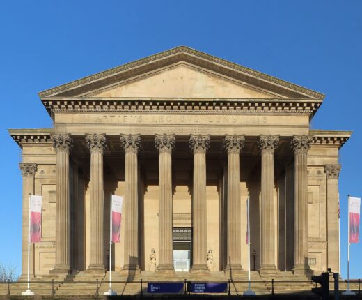 The south portico of St George's Hall, Liverpool: eight fluted Corinthian columns under a pediment inscribed Artibus Legibus Consiliis, against a deep blue sky