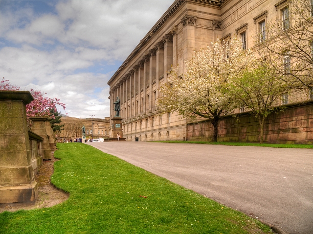 The long colonnaded rear elevation of St George's Hall in Liverpool seen from the lawns of St John's Gardens, with blossom trees in flower