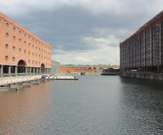 Looking along Stanley Dock in Liverpool: the red brick Titanic Hotel warehouse with its cast-iron colonnade on the left, the dark fourteen-storey Tobacco Warehouse on the right and narrowboats moored between