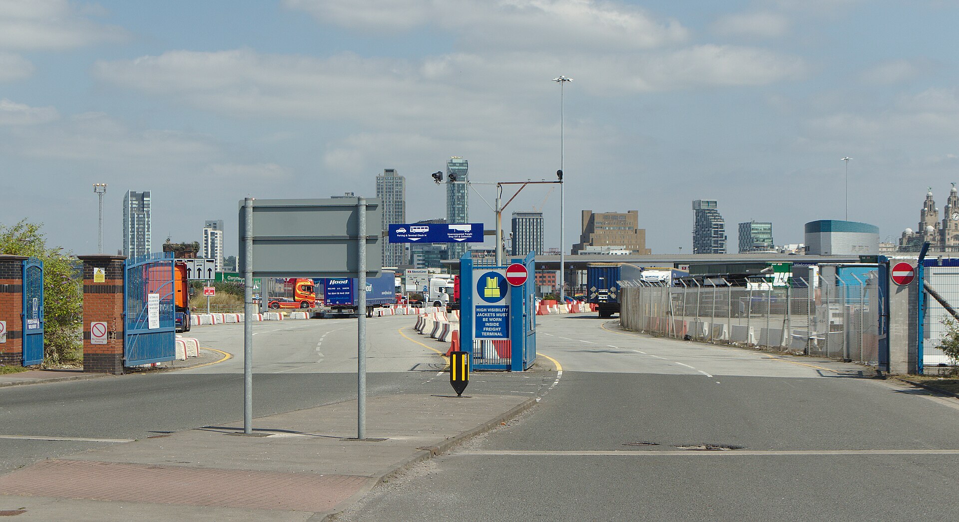 Liverpool to Belfast Ferry & Getting to Ireland from Liverpool 2 The road entrance to the Twelve Quays ferry terminal in Birkenhead, with blue gates, a sign for parking and terminal check-in, lorries in the freight area and the Liverpool skyline across the river behind