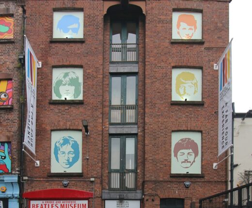 A tall red-brick building at 23 Mathew Street with portraits of the Beatles in its windows, banners on the facade and red doors painted with the band members' names