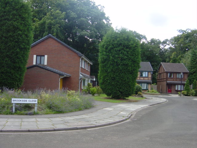 A quiet cul-de-sac of modern brick detached houses with neat hedges and trees, and a Brookside Close street sign on the grass verge