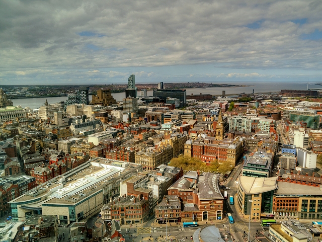 Best Views in Liverpool: Viewpoints, Towers & Skyline Spots 1 A wide view over Liverpool city centre rooftops, the Victorian clock tower of a church and modern towers, with the River Mersey and the Wirral beyond under a cloudy sky