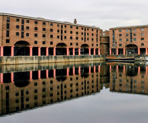 Liverpool History & Heritage: A Cultural Deep Dive 18 Red-brick warehouses and red columns at Liverpool's Royal Albert Dock reflect in calm water beside moored boats.