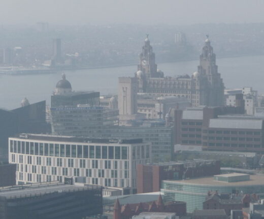 A hazy view over Liverpool city centre rooftops towards the Royal Liver Building and the River Mersey, seen from high above