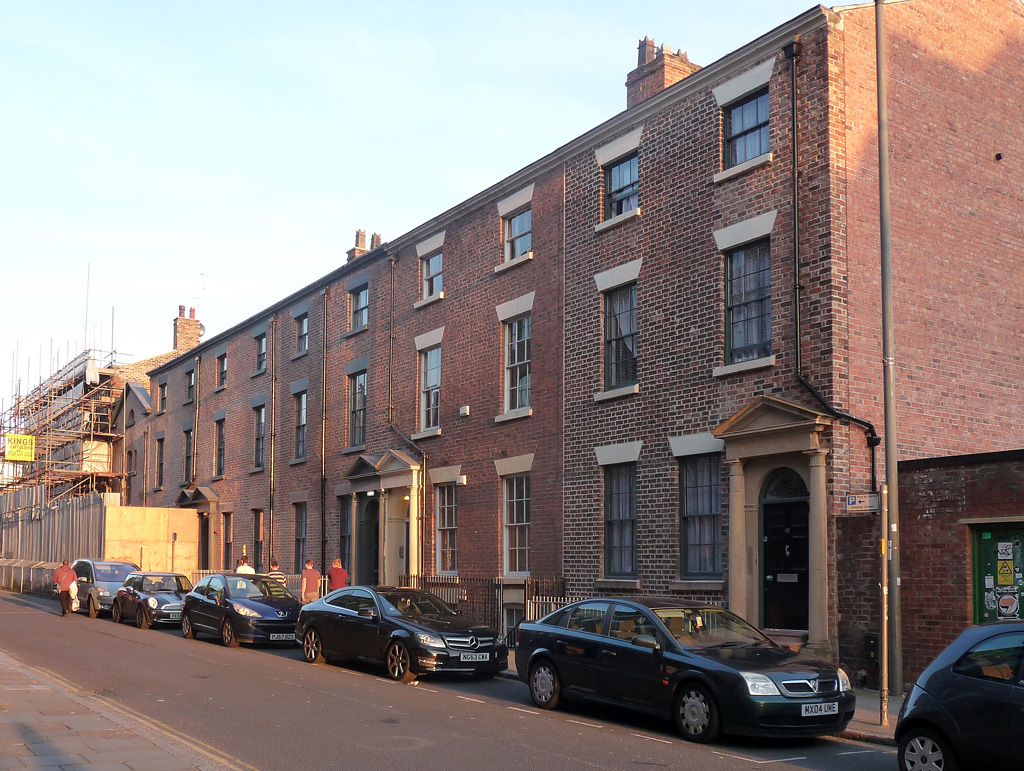 A long terrace of three- and four-storey red brick Georgian houses on Seel Street with sash windows and a pillared doorway, cars parked along the kerb