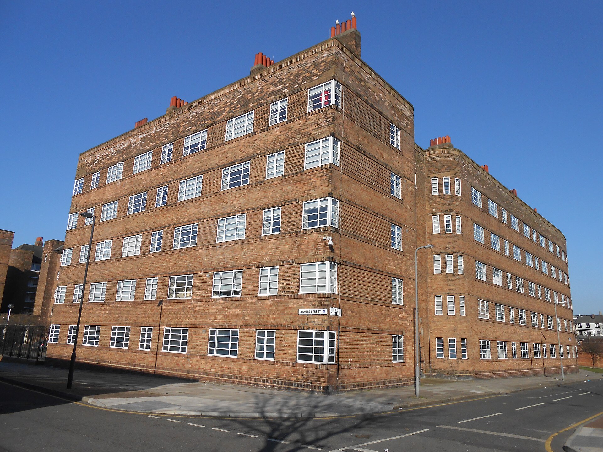 A large block of brown brick flats with rows of white-framed windows and chimneys, under a blue sky