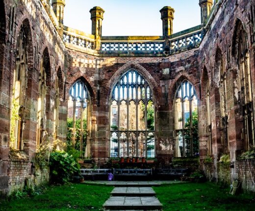 Inside the roofless shell of St Luke's Bombed Out Church in Liverpool, with empty Gothic windows, red sandstone walls, a lawn and a paved path