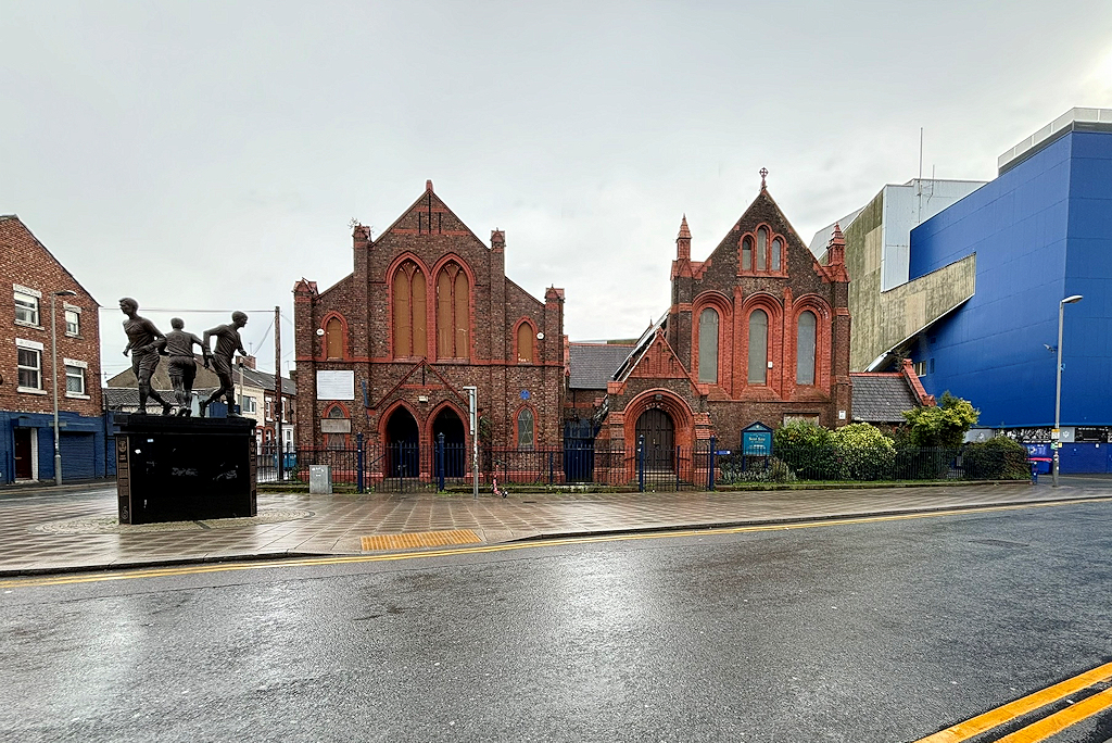Anfield, Everton & North Liverpool: What's There Beyond the Stadiums 2 The red brick Victorian St Luke's Church on Goodison Road beside the blue-clad stand of Goodison Park, with a bronze statue of three footballers on a plinth in front