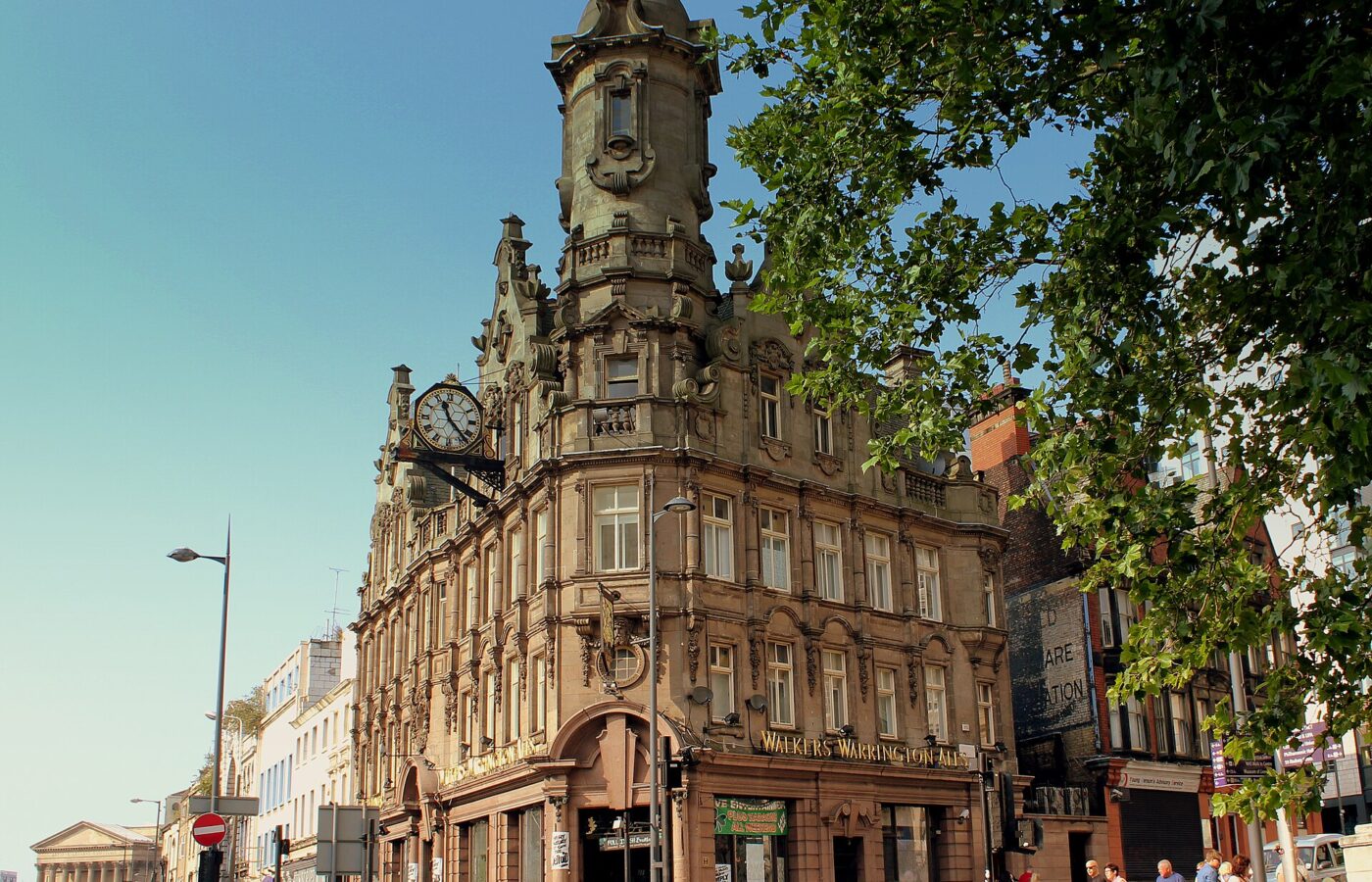 The ornate Vines pub on Lime Street, Liverpool, with a clock, a domed corner tower and carved stonework, and people walking past in sunshine